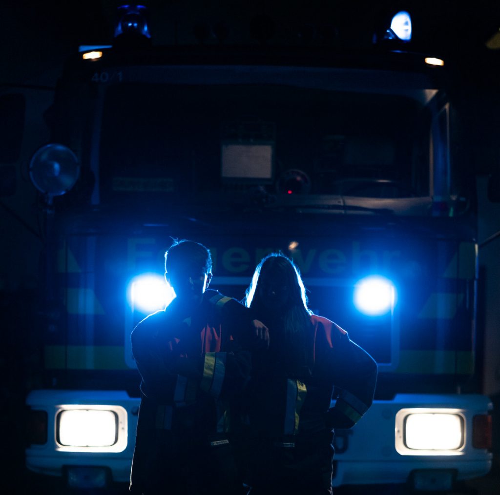 Zwei Jugendliche posieren vor beleuchtetem Feuerwehrfahrzeug
